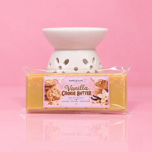 A packaged bar of vanilla cookie butter scented wax melt from Sparkle & Scents, placed in front of a white ceramic wax warmer on a pink background.