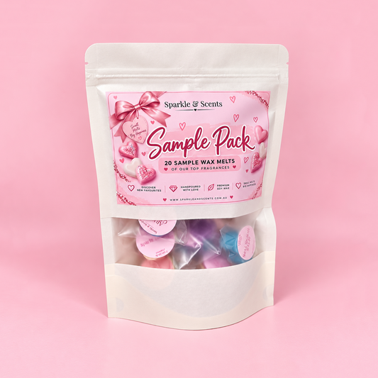 A white stand-up pouch of Sparkle & Scents 'Sample Pack' containing 20 sample wax melts in various pastel colors, visible through a clear window on the lower half. The packaging features a pink label with hearts and bows, set against a solid pink background.